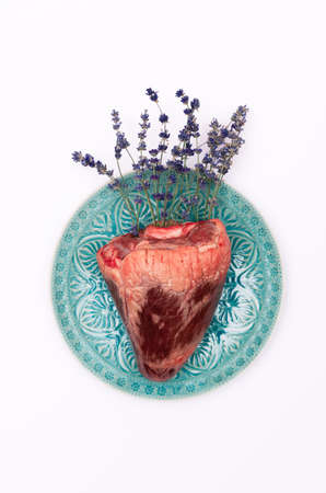 Top view of real animal heart with lavender flowers on a turquoise plate and white background.の写真素材