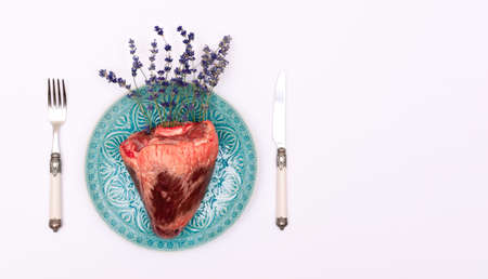 Top view of real animal heart with lavender flowers on a turquoise plate and white background.の写真素材