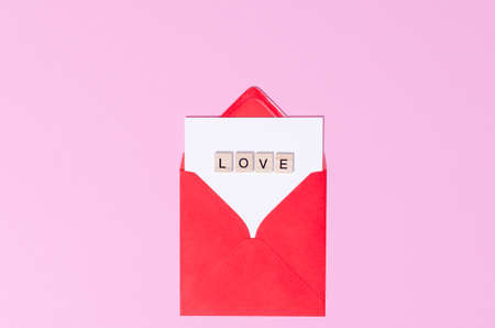 Top view of a red envelope with word love on a pink pastel copy space background. St Valentines Day letter concept.の写真素材