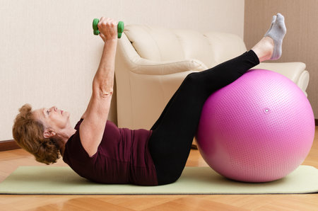 Senior woman exercising with dumbbells and fitness ball at home, healthy lifestyle, active elderly...
