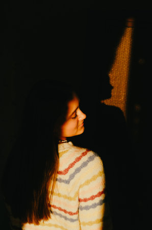 Beautiful dreamy young girl enjoying sunset light in her dark room.