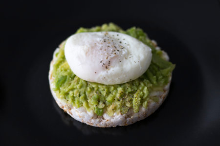 Breakfast. Egg Poached and Avocado Sandwich on a plate with a dark black background.