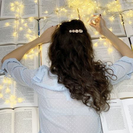 Top View of Young Woman Lying on Pile of Open Books with Swag