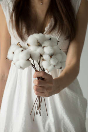 Woman in a dress holds in her hands a bouquet of natural twigs with cotton blossoms.の写真素材