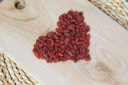 Goji berries arranged in the shape of a heart on a light wooden board.