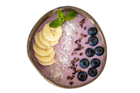 Smoothie bowl with fresh blueberries, coconut flakes, banana, cocoa beans and mint. Top view on an isolated white backgroundの写真素材