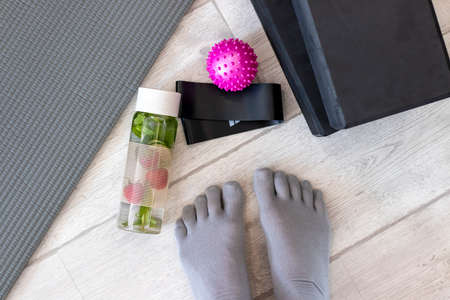 A girls feet in toe socks got ready to exercise on a mat with tape, a ball, yoga blocks and cucumber water.の写真素材