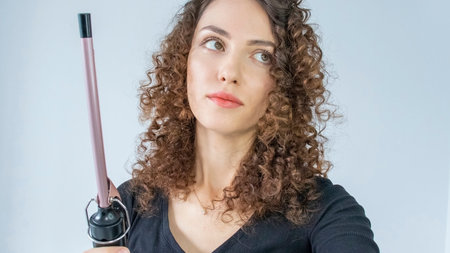 Curly Hair. Beautiful brooding woman looking up with curly hair, curling her hair, using curling tongs to get fine curls. Hairstyles and hairdressing tools.の写真素材