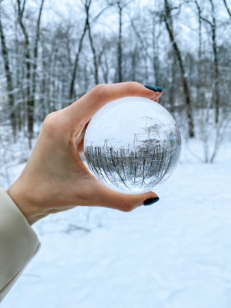 Ecology in winter. A transparent ball in a female hand in a winter forest with snow. Beautiful cold landscape. Ecotourism.の写真素材