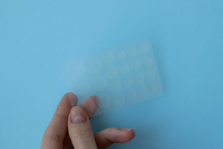 Pimple patch for oily and problematic skin in a woman's hand on a blue background.