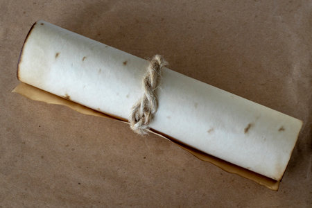 Ancient scroll rolled out of beige paper, tied with a rope on a brown background.の写真素材