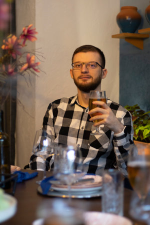 Enjoying a cold and fresh beer. A view of a handsome young man with a beard, wearing glasses for vision, drinking beer. Relaxing after work in a restaurant.の写真素材