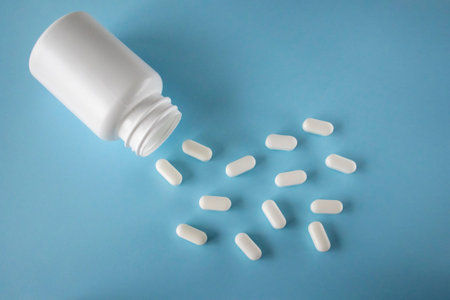 White pills and white jar on blue background, flat view from above. Pills for heart health. The...