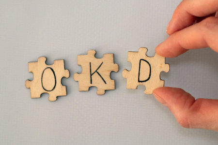 Obsessive compulsive disorder. Text lettering OCD handwritten on wooden puzzles. A womans hand assembles the puzzle.の写真素材