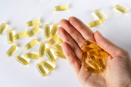 Fish oil in a womans hand on a white background with scattered capsules.の写真素材