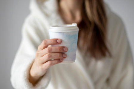 A woman holding a plastic coffee cup with a delicate watercolor drawing in her hand at homeの写真素材