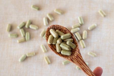 Vitamin from broccoli sulforaphane in capsules in a wooden spoon on a beige background. Tablets and medicines in greenの写真素材