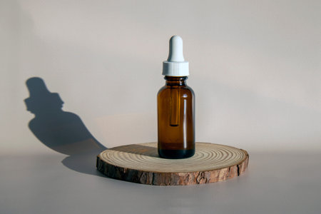 Mock-up of a brown glass bottle with an eyedropper. Serum or oil for face and body. Round wooden podium on beige background.の写真素材
