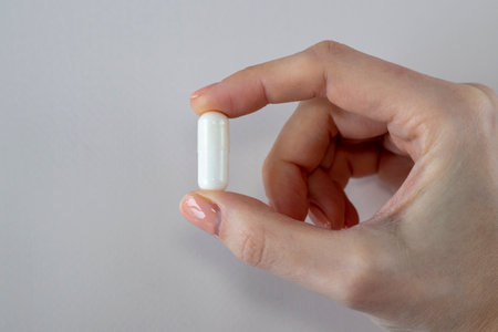 A large white capsule with a supplement in a womans hand against a white background. Pills, medicines and vitamins.の写真素材