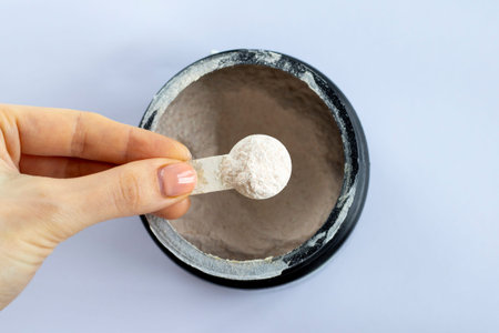 Black jar with electrolytes in measuring spoon in womans hand on white background, top view