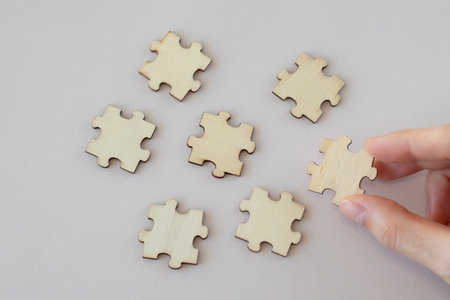 A womans hand holds a wooden puzzle next to others scattered on a beige background. Mock Up