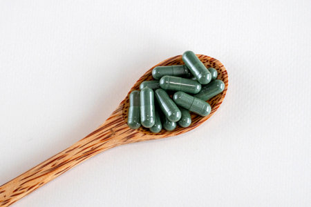 Green capsules with spirulina or chlorella supplements in a wooden spoon, top view. Dietary supplements.の写真素材