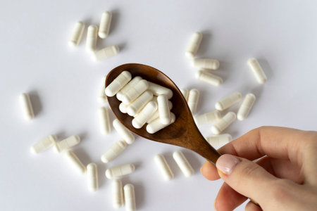 Lots of pills on a white background in a wooden spoon. Nutritional supplements with enzymes, vitamins, medications or pills.の写真素材