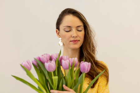 Portrait of a beautiful young fashionable woman with a bouquet of pink tulips on a beige background, selective focus. Celebration of Womenの写真素材