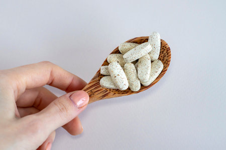 Oval beautiful beige stained medicines in a wooden spoon in a womans hand. Vitamin complex for...