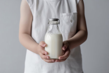 Childs Hands Holds Bottle Of Milk Against White Backgroundの素材