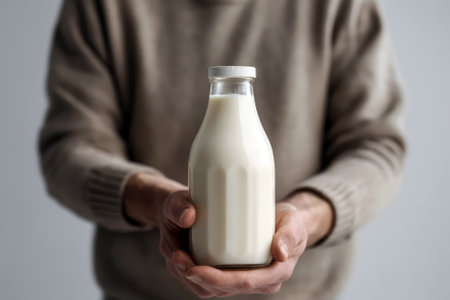 Mans Hand Holds Bottle Of Milk Against White Backgroundの素材