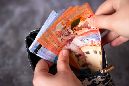 Hands holding Thai banknotes in a black purse on a dark background