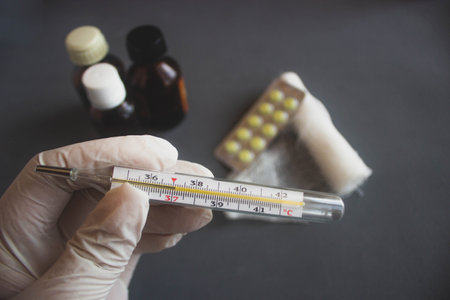 thermometer in hand on a black background with pills and plasterの写真素材