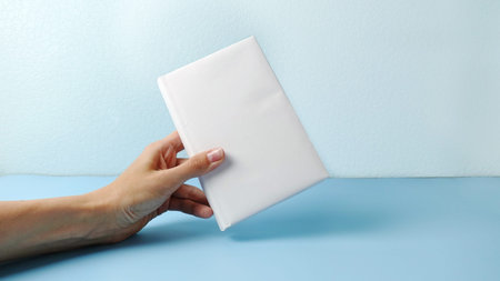 A mockup of an close book in womans hand isolated on blue .mockup with shadow. book endpaper. Blank...