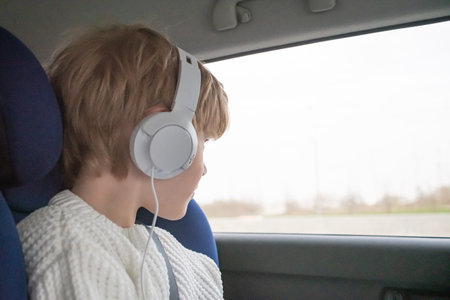 A boy in white headphones is sitting in the car, The concept of spending time on long trips. How to entertain a childの写真素材