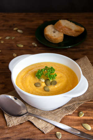 Pumpkin cream soup in a white bowl with croutons stands on a wooden table. Side view, vertical orientationの写真素材