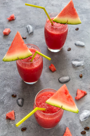 Three watermelon smoothies in glasses with ice on a gray concrete table. Vertical orientation