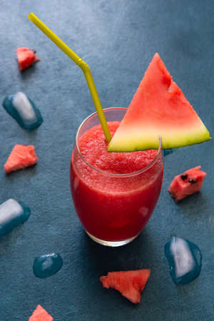 Watermelon smoothie with a slice of watermelon with ice on a blue table. Vertical orientationの写真素材