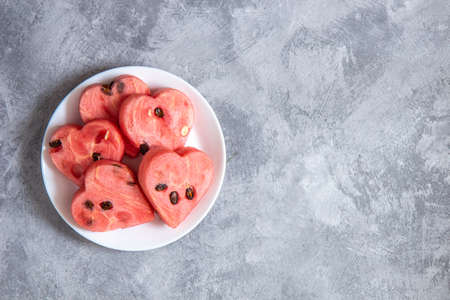 Heart shaped watermelon slices on a white plate on a concrete surface. Top view, copy space.の写真素材