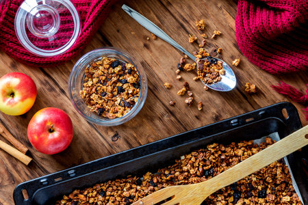 Apple granola with honey and spices on a baking sheet and in a glass jar on a wooden table. View from aboveの写真素材