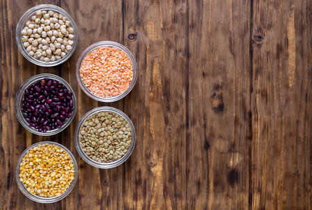 Various legumes in bowls on a wooden background.の写真素材