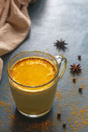 Traditional Indian turmeric latte drink with spices on a dark blue background with sprinkled spices. Vertical photo, place for text.の写真素材