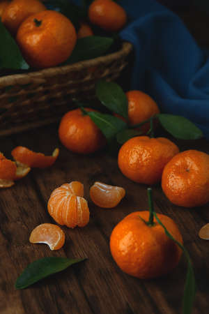 Mini tangerines with leaves in a basket and on a wooden table. Vertical photo in low key.の写真素材