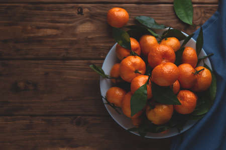 Tangerines with leaves in a plate on a wooden background. Top view, place for text.の写真素材