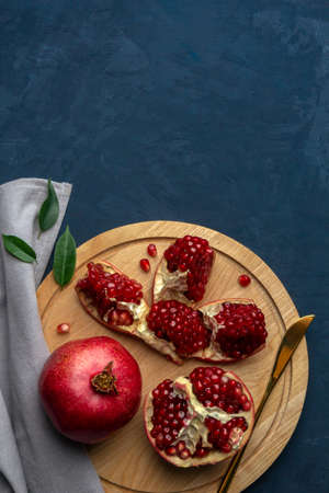 Sliced pomegranate on a cutting board with a knife on a dark blue background. Top view, copy space.の写真素材