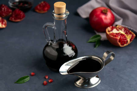 Pomegranate sauce in a bottle and gravy boat with grains and pieces of pomegranate on a dark background. Side view, selective focus.の写真素材