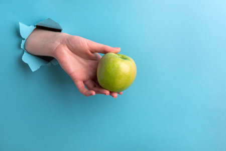 The green apple in the womans hand is made of a hole on a turquoise background