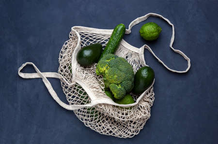 Reusable bag with green vegetables on a dark blue background. Mesh string bag, plastic free concept, top viewの写真素材