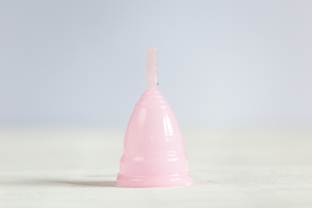 Pink menstrual cup lies on a white vintage wooden background. Selective focus, copy space.の写真素材