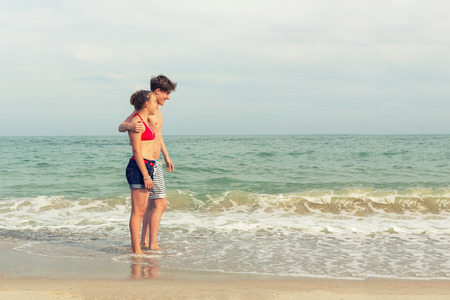 Two teenagers: a girl and a boy with blond hair, dressed in a swimsuit are walking on a sea beach. Copy space.の写真素材